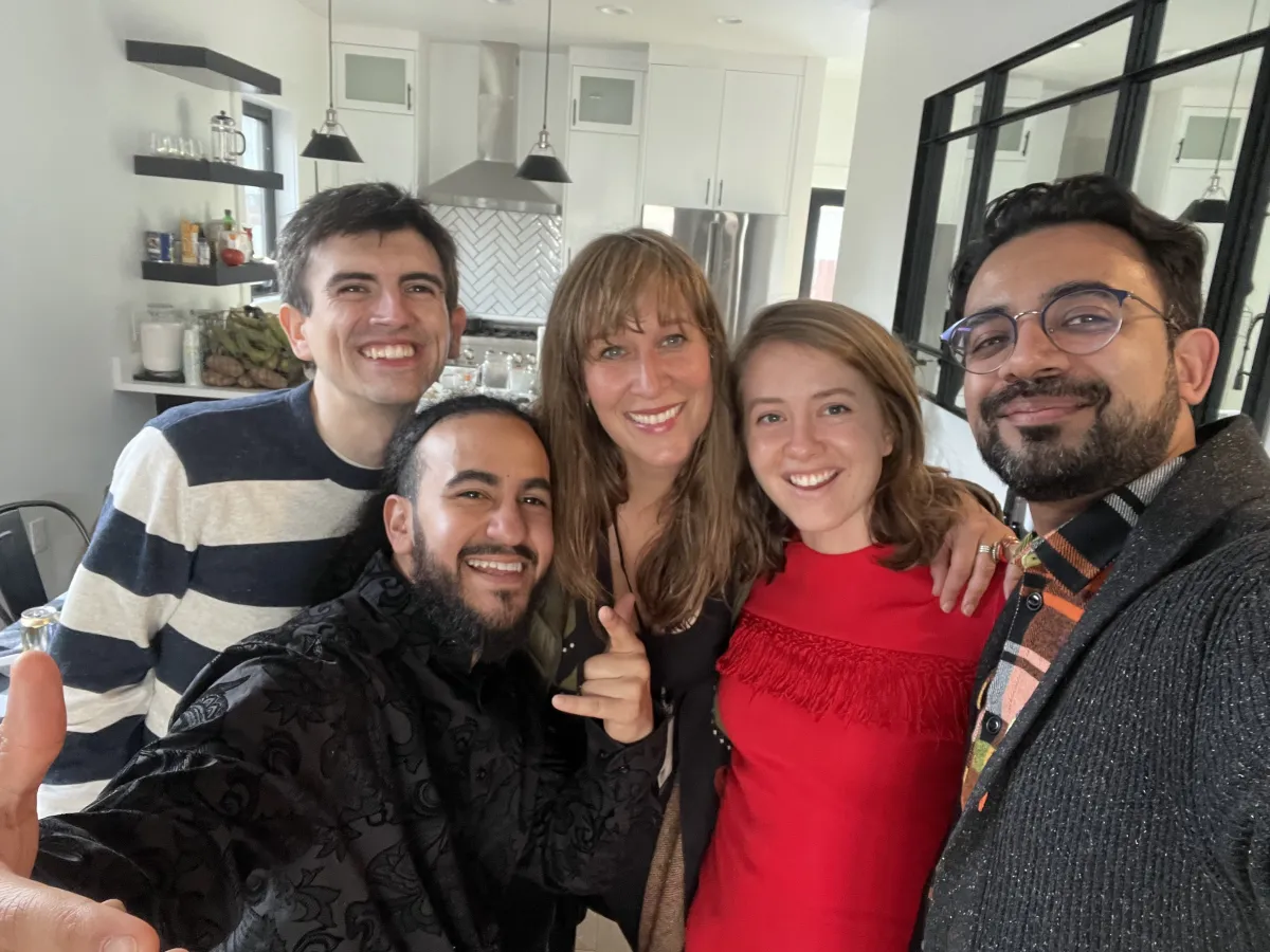 A selfie of three men and two women, all smiling and dressed nicely, taken in a spacious, white kitchen