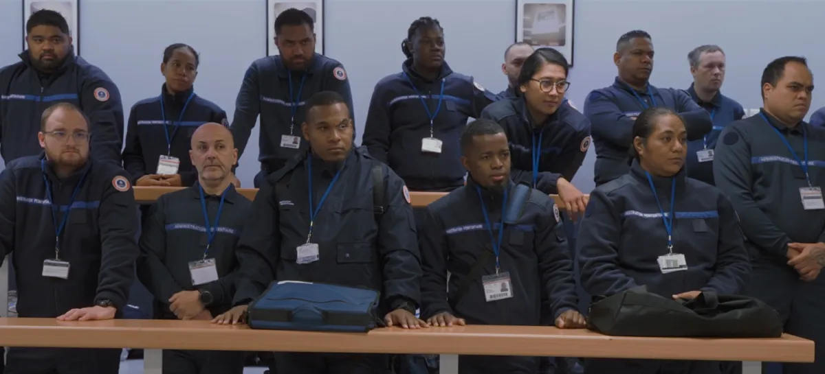 14 uniformed guards stand in two rows behind long tables