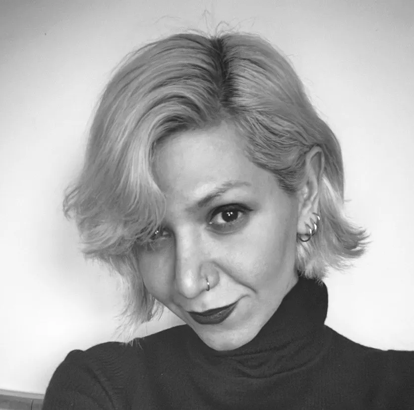Black and white headshot of a light-skinned woman wearing a dark turtleneck shirt with lightened short hair falling on her face