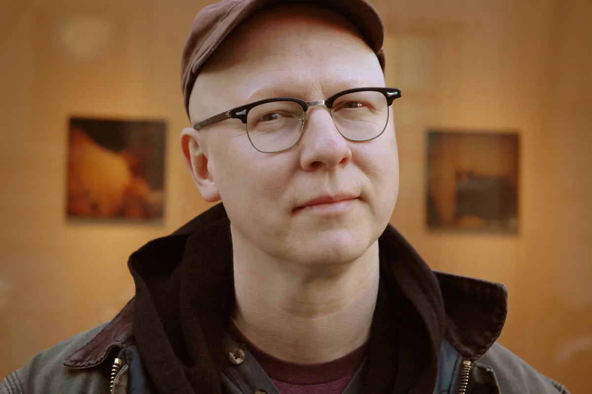Headshot of a white bald man with glasses and a hat 