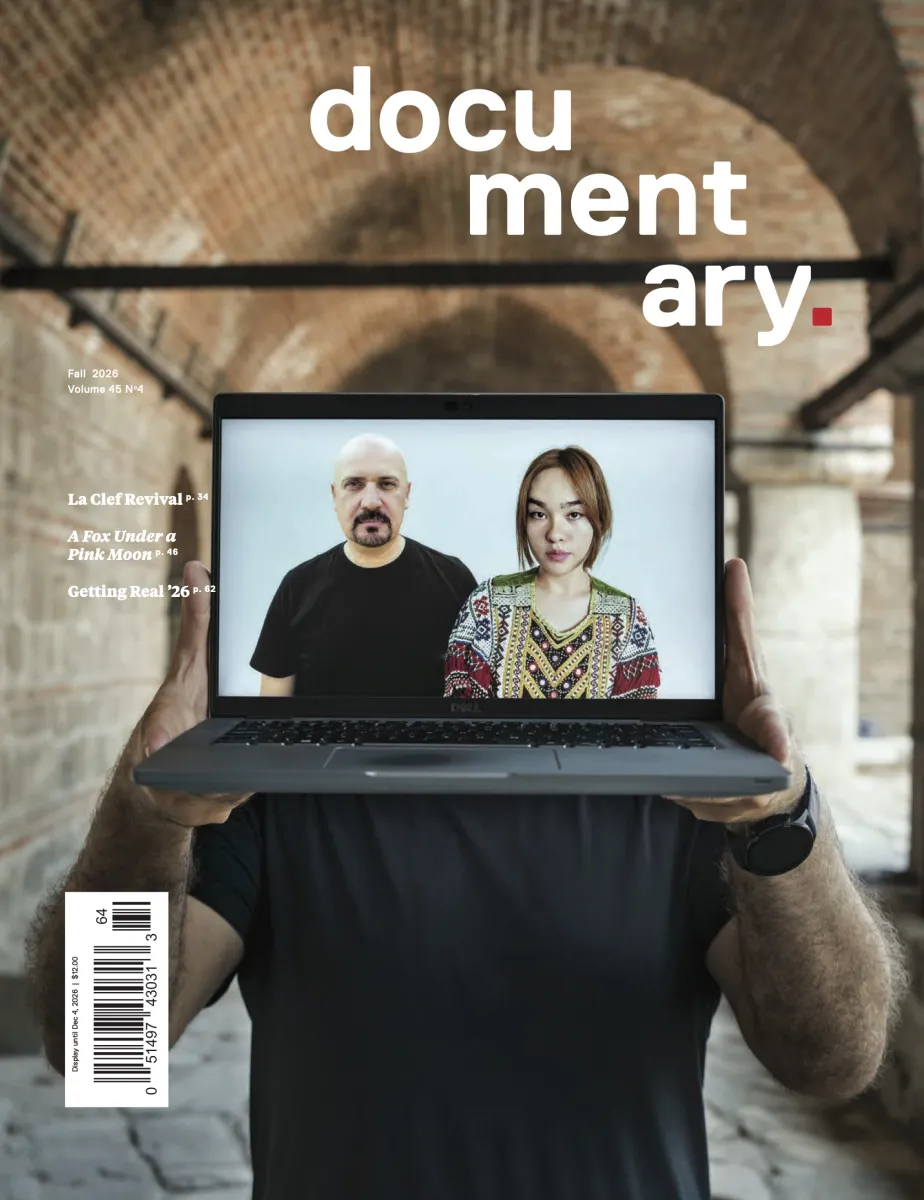 Cover of Documentary magazine featuring a light-skinned man in a black t-shirt outside in a red-bricked building holding a laptop that obscures his face which features a photo of a bald middle-aged man in a black t-shirt in a goatee, and a young auburn-haired young woman with a bright, patterned top