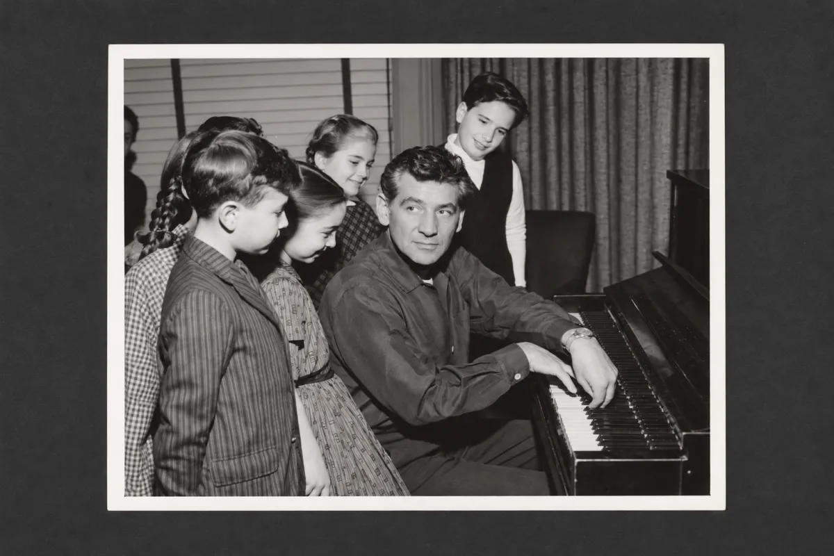Leonard Bernstein playing the piano with a group of young children.