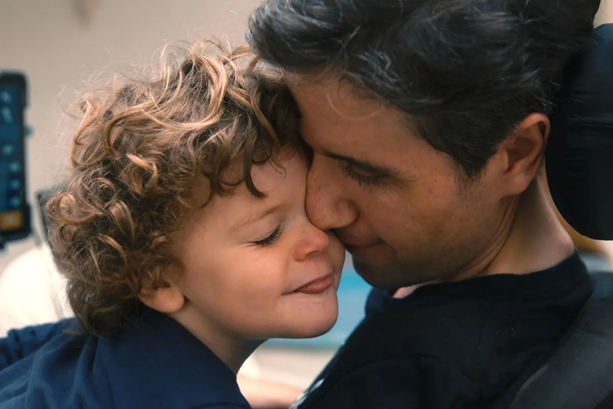 Ady Barkan is a white male American activist seen here sharing an affectionate moment with his child. Image from Nicholas Bruckman’s ‘Not Going Quietly.’ Courtesy of Michael Dwyer/POV. 