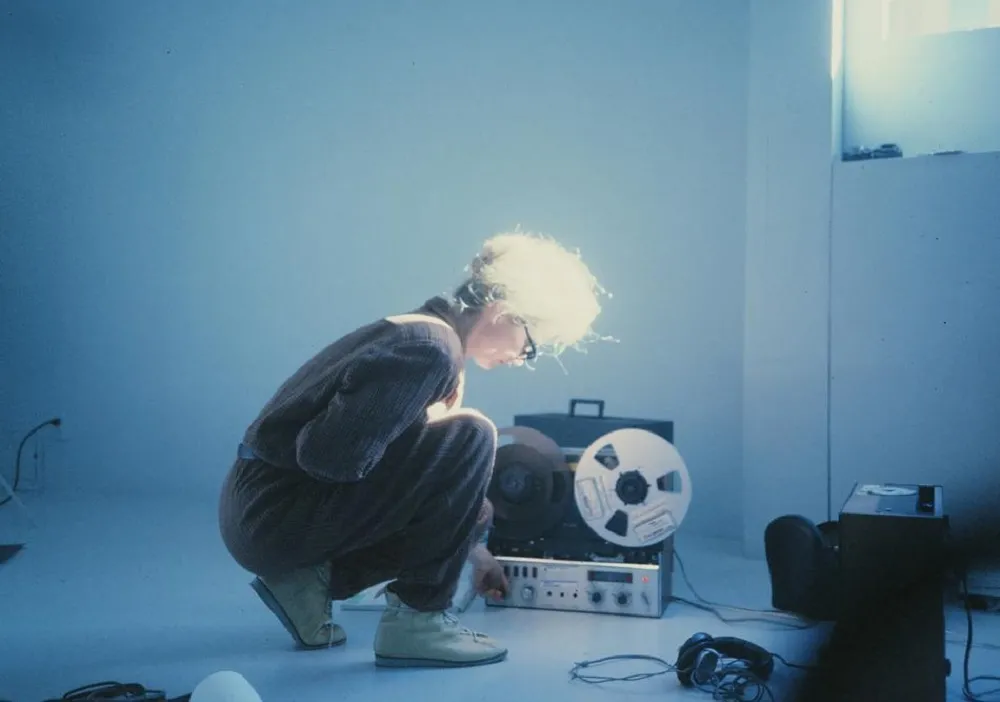 Maryanne Amacher is a white American composer and installation artist. She is wearing a gray jumpsuit and working in a room with musical equipment. From Lisa Rovner’s ‘Sisters with Transistors.’ Courtesy of Metrograph.