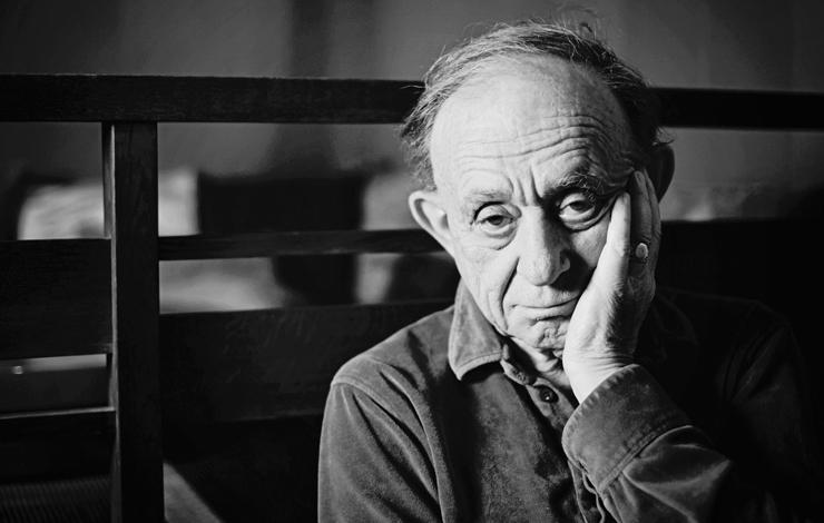 A black-and-white photo of Frederick Wiseman, an older man sitting with his head resting on his hand. 