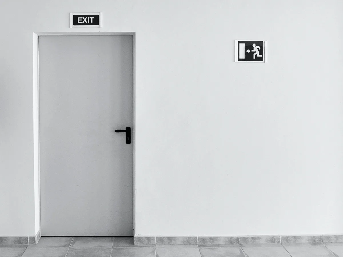 A white door with an exit sign above it and an exit symbol beside it.