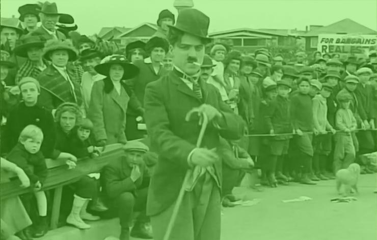 A green overlay on a photo of Charlie Chaplin. In Chaplin's first film, 'Kid Auto Race at Venice' (1914) Mack Sennett's crew went to Venice, California, to shoot a real event.