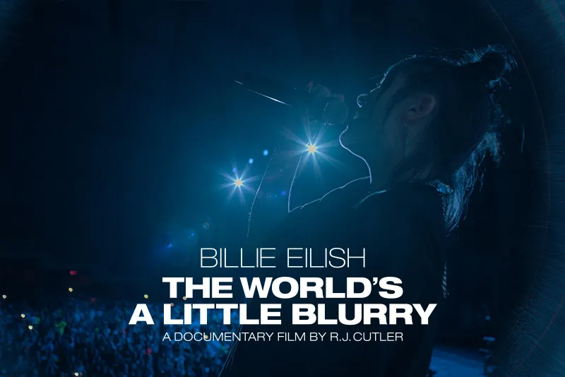 Billie Eilish singing to a crowd with blue lights shining in the background