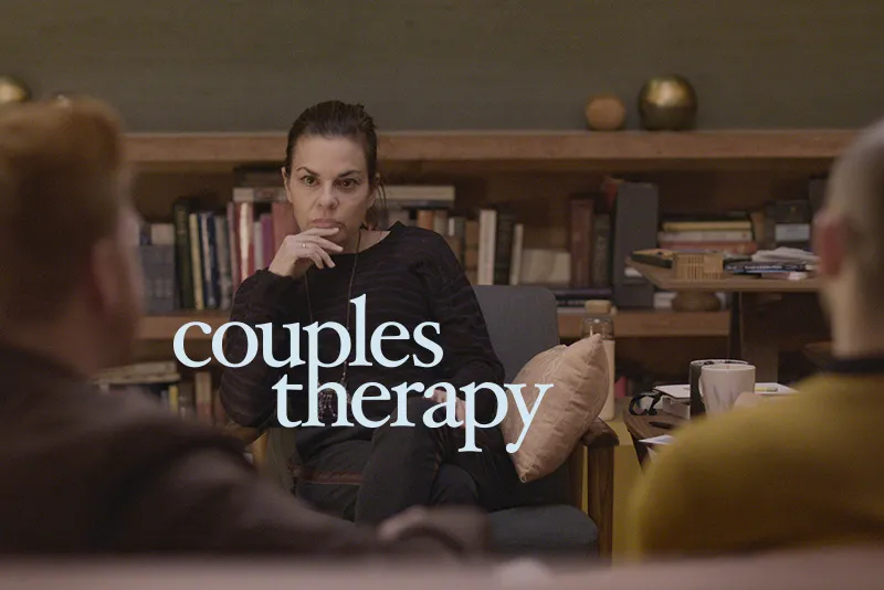 Two adult is out of focused in the foreground facing an adult female therapist