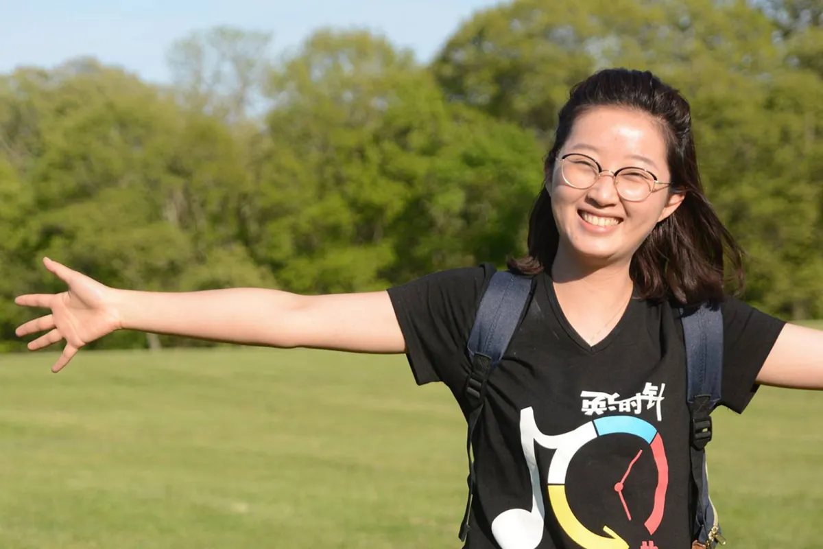 A young Chinese woman is smiling, holding her arms out on a grassy lawn