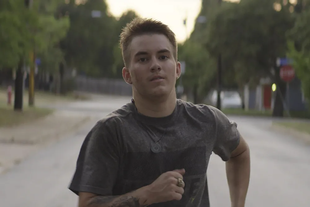 A man with white skin and short blond hair runs down a street.