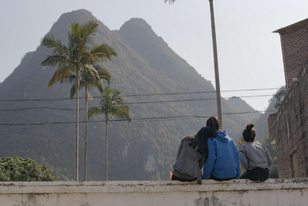 Three people sit on a ledge and stair at a mountain.