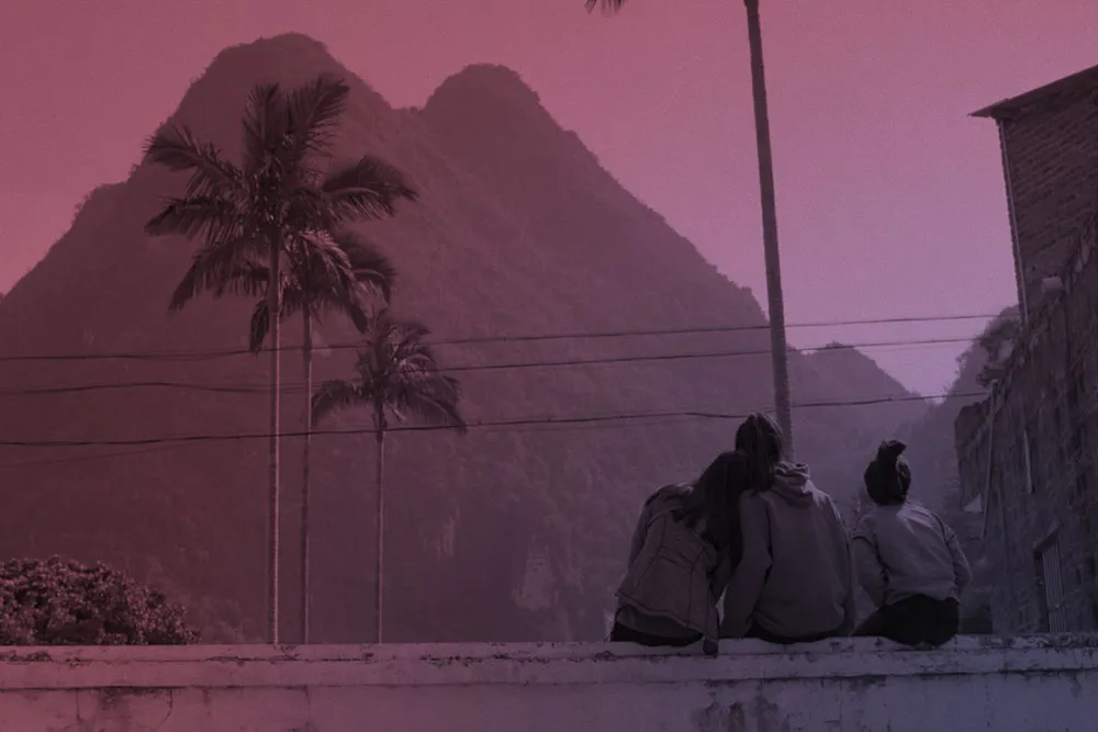Three people sit on a ledge and stair at a mountain.