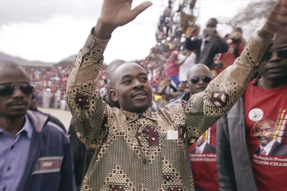 A man with Black skin and a patterned shirt addresses a large crowd.