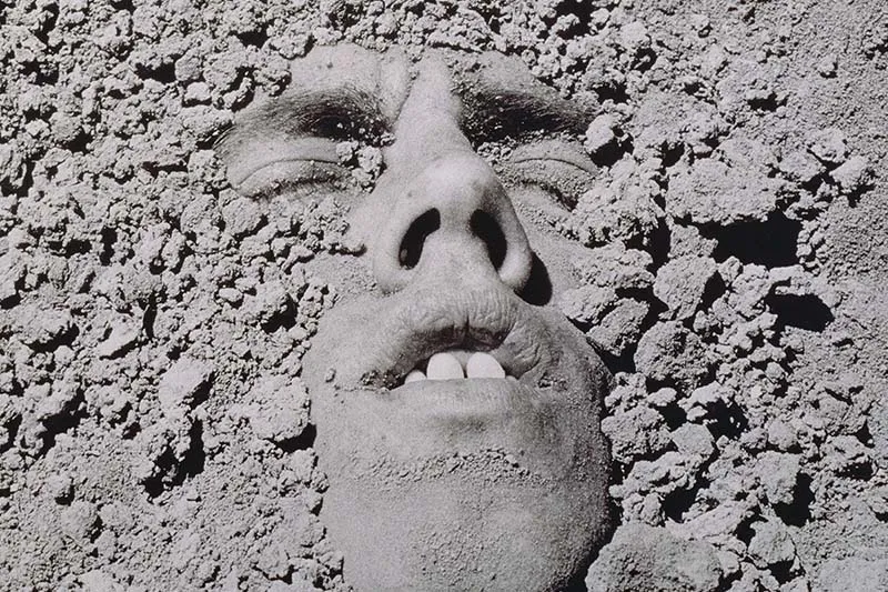 A black and white portrait of a white man submerged in dirt. David Wojnarowicz, Untitled (Face in Dirt), 1991. © Estate of David Wojnarowicz. Courtesy of the Estate and P·P·O·W.