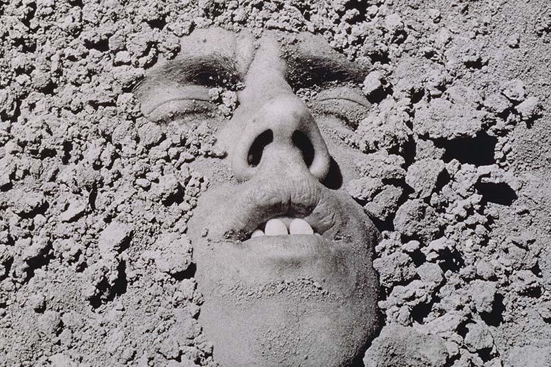 A black and white portrait of a white man submerged in dirt. David Wojnarowicz, Untitled (Face in Dirt), 1991. © Estate of David Wojnarowicz. Courtesy of the Estate and P·P·O·W.