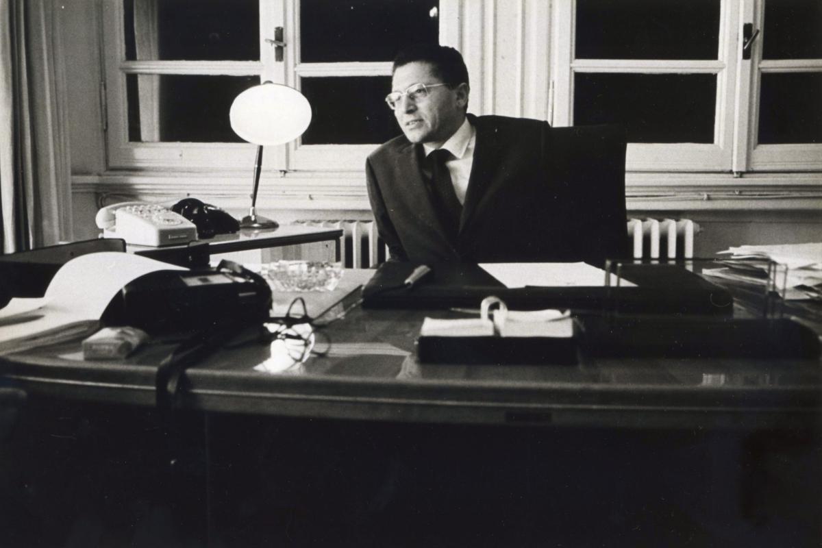 Kikhia leans over his mid-20th century style desk