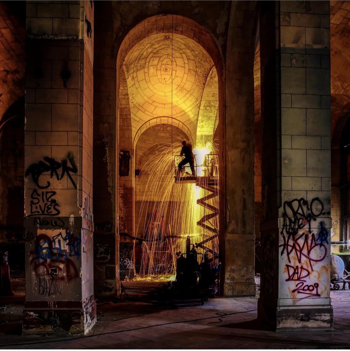 a man welds in the graffitied arches of what appears to be an old church. 