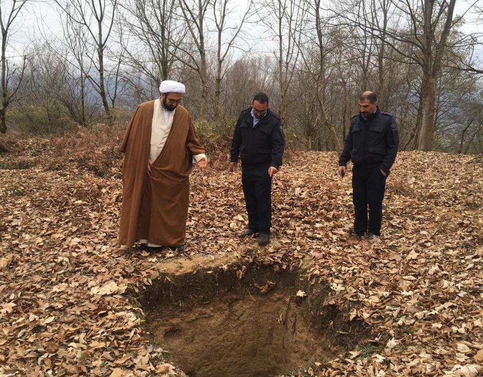 Three men stand over a hole in the ground, pointing into the dirt.