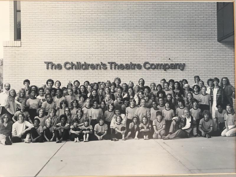 A black and white class photo in front of a building named "The Children's Theater Company"