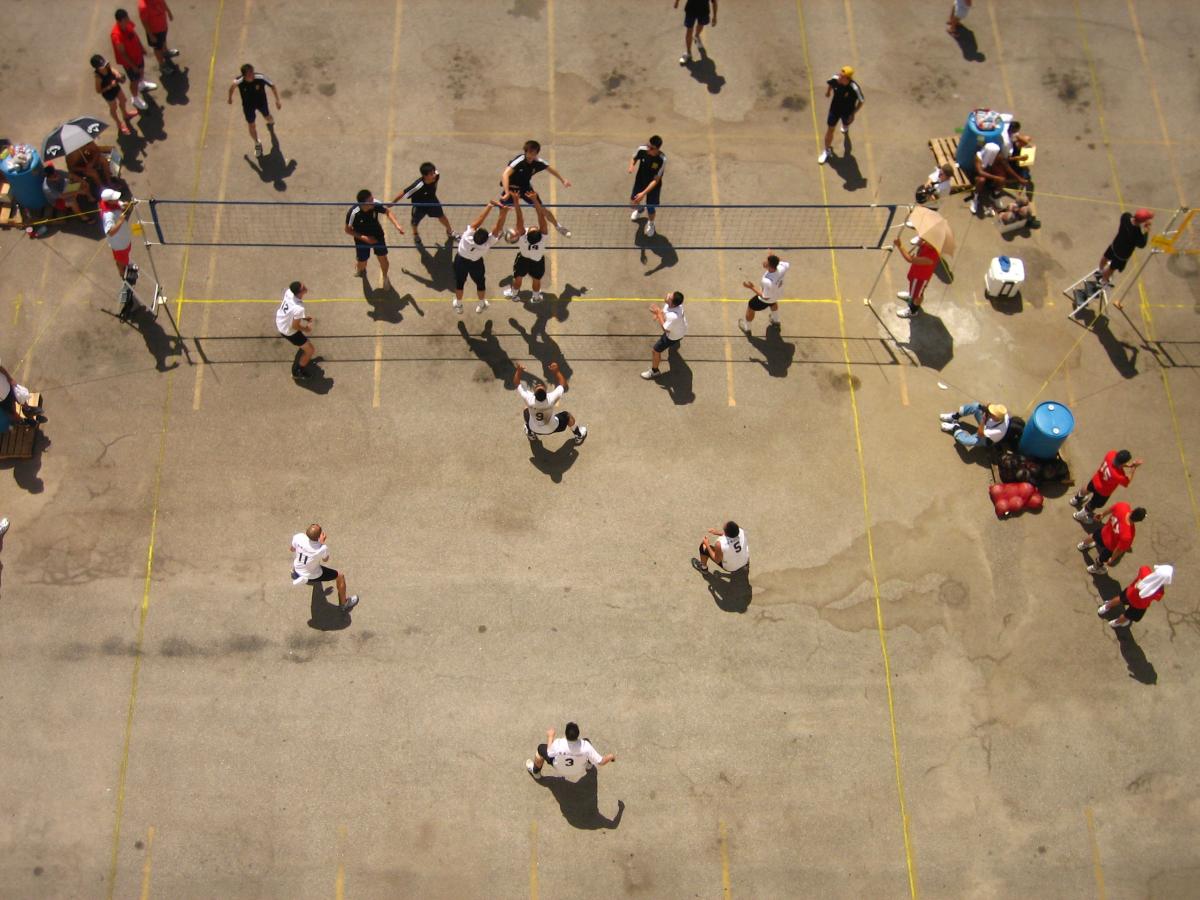 We look down from above at a  crowd of Asian-American men playing street volleyball.