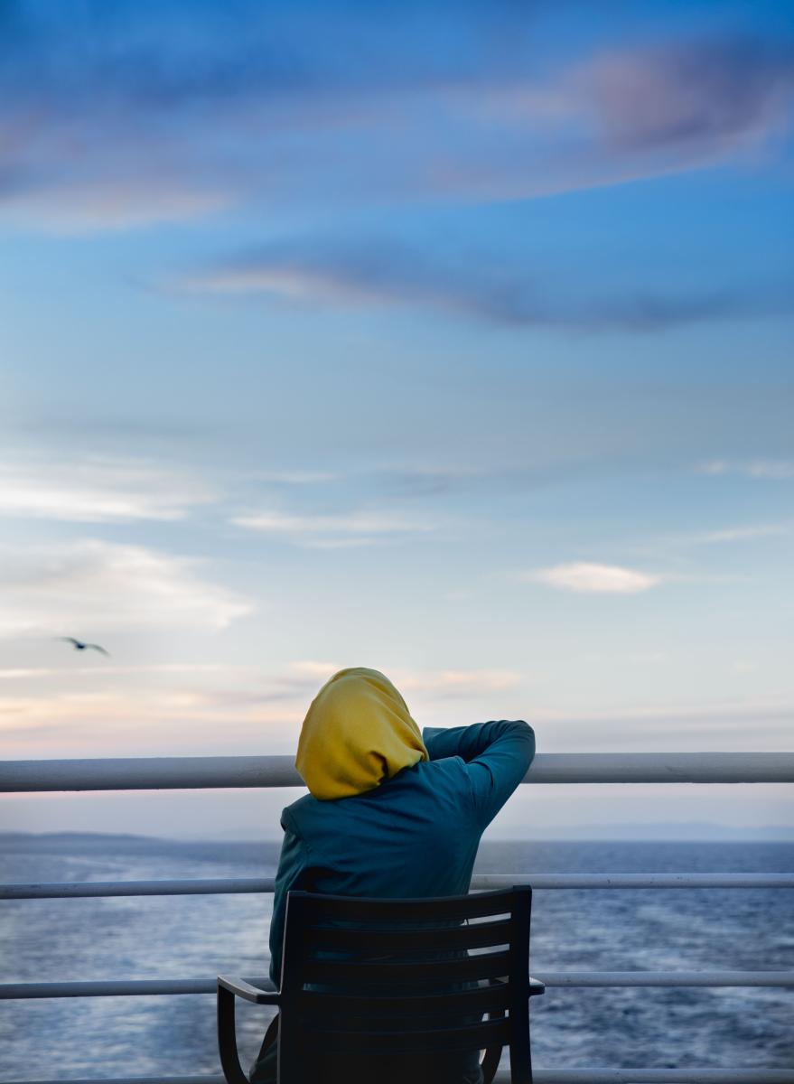 An individual in a yellow hijab sits in a chair in the stern of a boat before the ocean