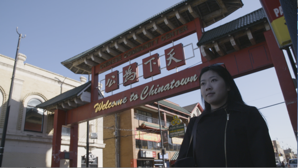 Chinese American woman stands in front of the gate of New York City's Chinatown. 