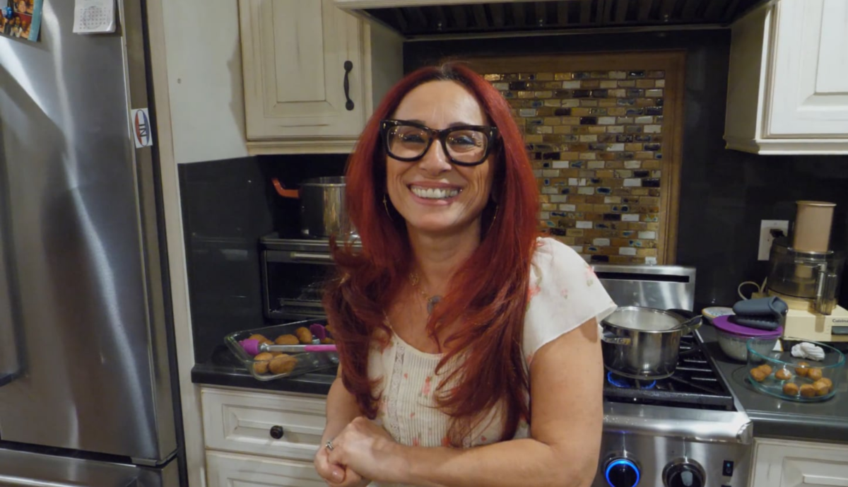 A red-haired Armenian-American smiles at the camera in a home kitchen.