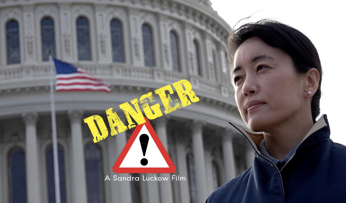 An Asian woman in a windcoat stands in front of the US Capitol.