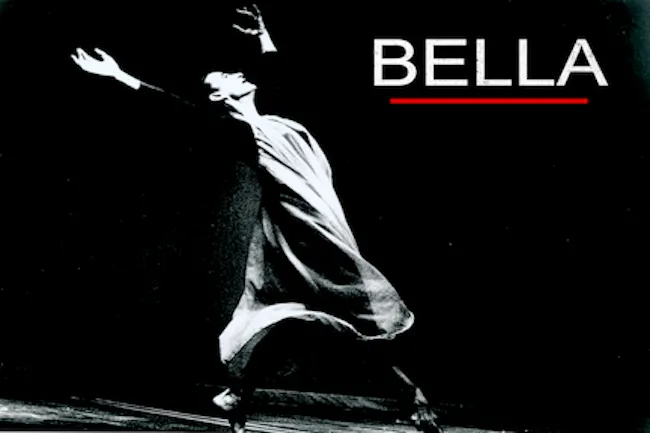 Black and white photo of female dancer in a white flowing dress with her arms raised in the air