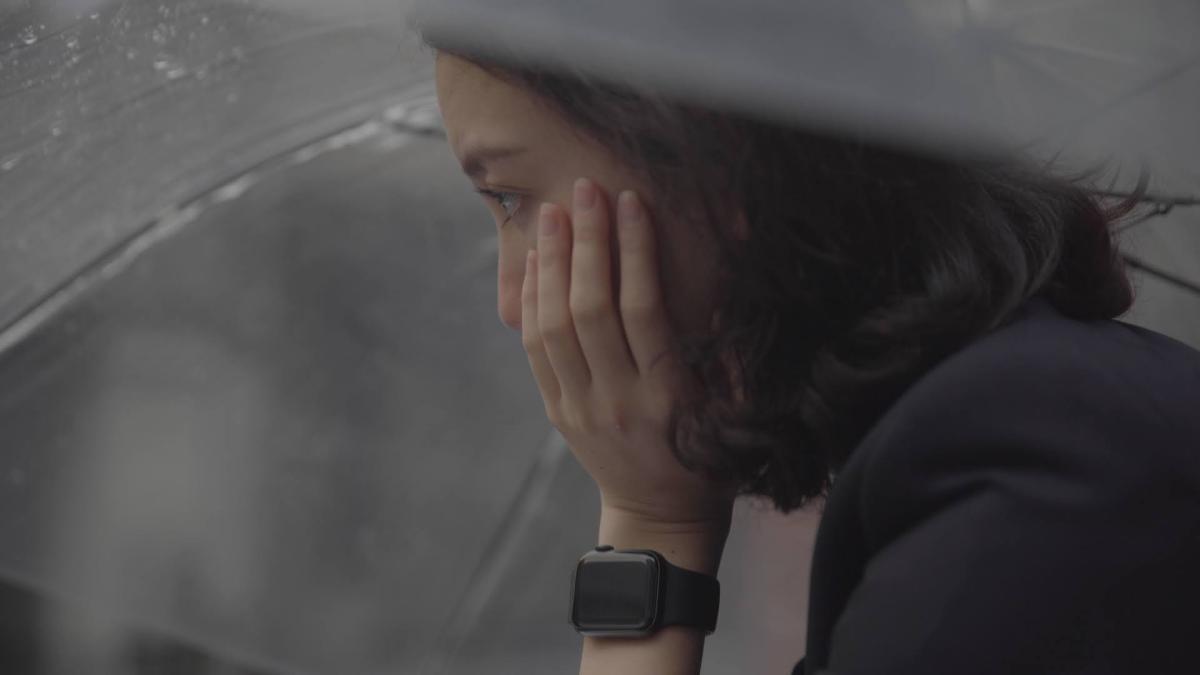 Film still of a pensive Shiori under an umbrella, face in hand
