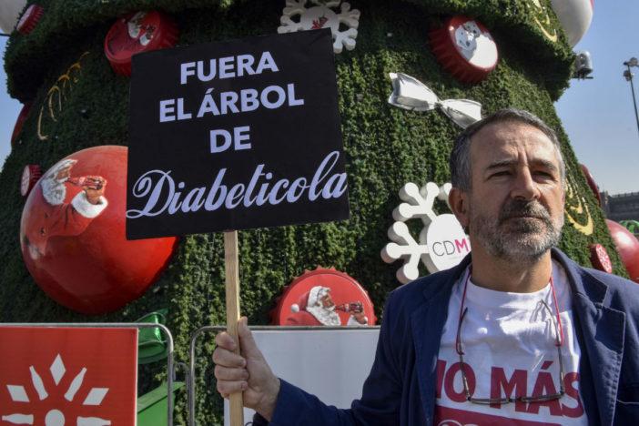 A Mexican activist stands in front of a Christmas tree with a sign.