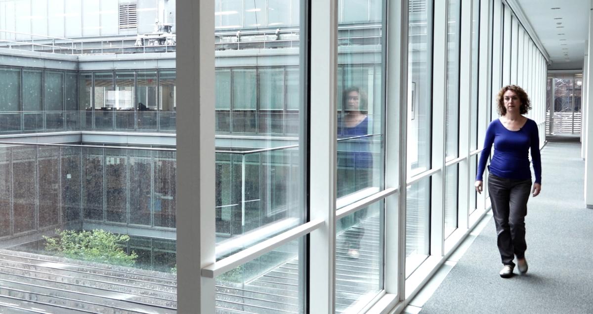 A woman is walking through a glass hallway in an art museum.