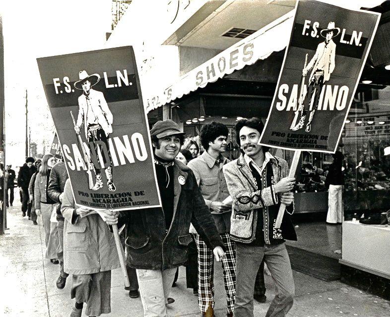 Black and white photo of protesters holding a F.S.L.N. poster.