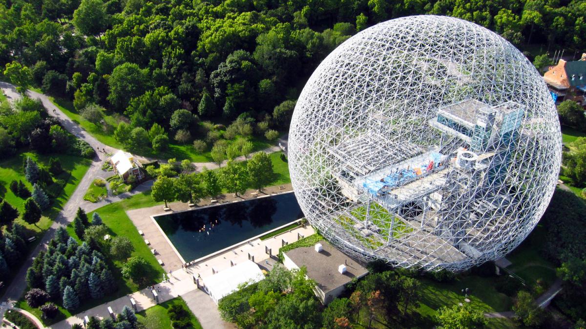A geometric steel dome sits on a green landscape. 