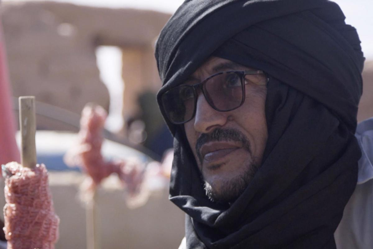 A man in a black headscarf and glasses looks into the distance.