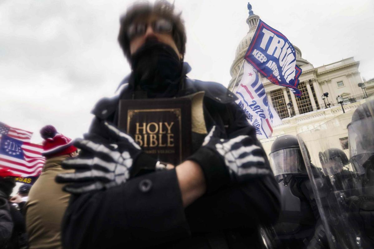 January 6, 2021. A ghoulish figure clasps a Bible amidst the crowd of insurrectionists on the Eastern Front of the U.S. Capitol.