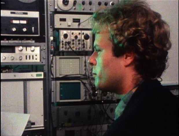 Ken Kelley stares in profile, surrounded by towers of sound recording equipment. 