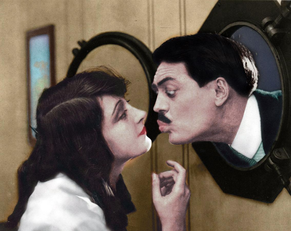 Max Linder is kissing a woman in a movie scene.