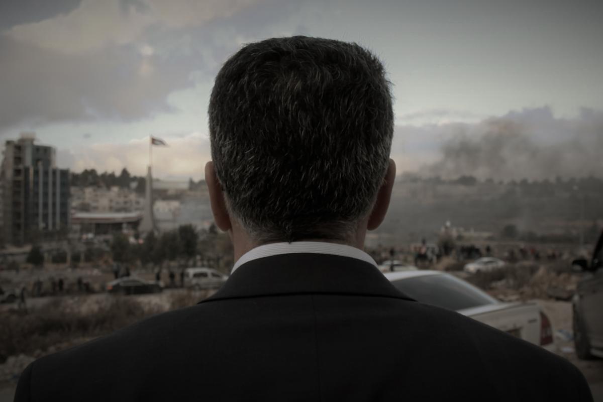 Main subject of film looks away from camera towards his town in a suit.