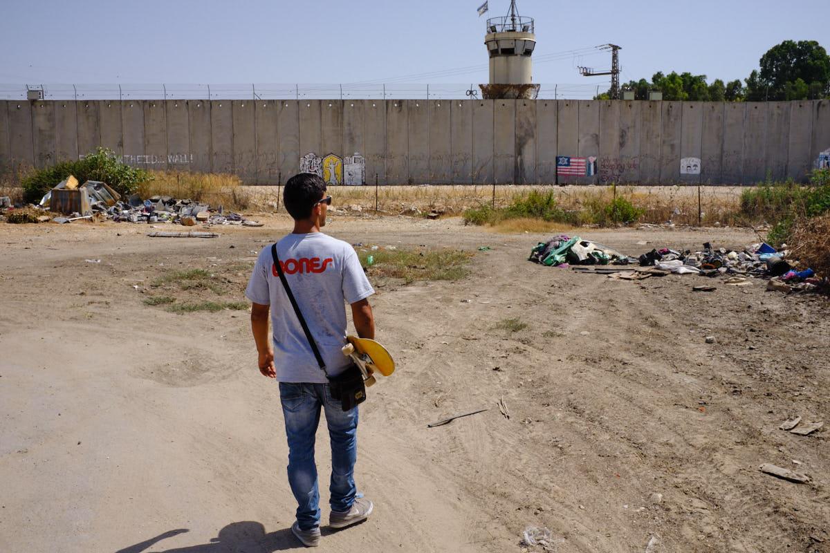 Omar Hattab approaches the separation wall in his hometown of Qalqilya, with barbed wire and a guard tower across the top.