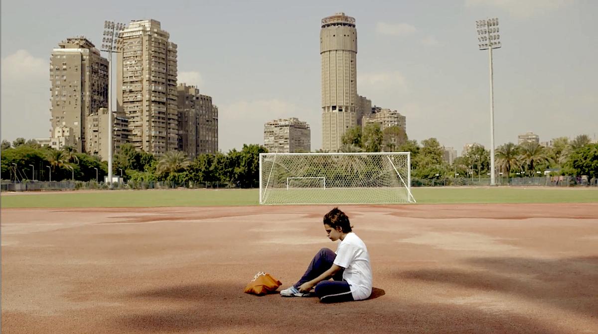 A teenager sitting in the middle of a soccer field.