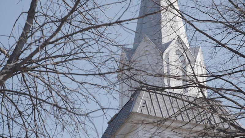 Photo of a white steeple partially hidden behind bare tree branches. 