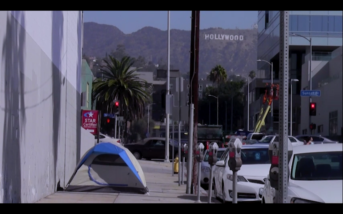The tent of an unhoused person on the street with the hollywood sign in the background.