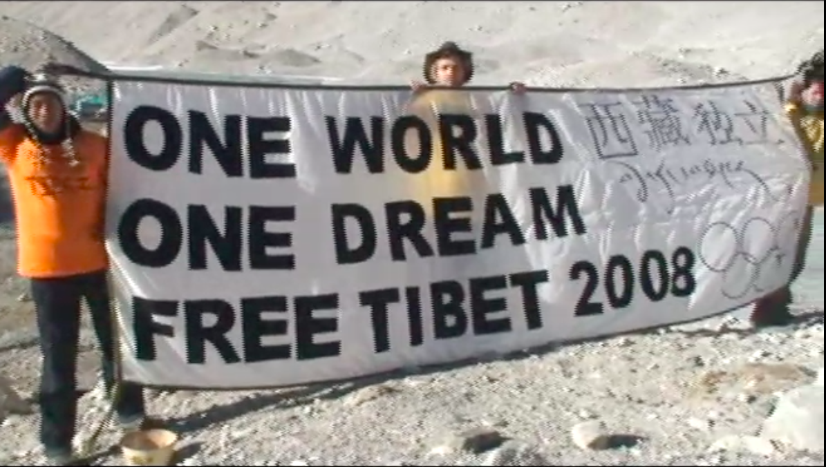 three men in orange jackets hold a banner which reads "one world, one dream, free Tibet 2008"