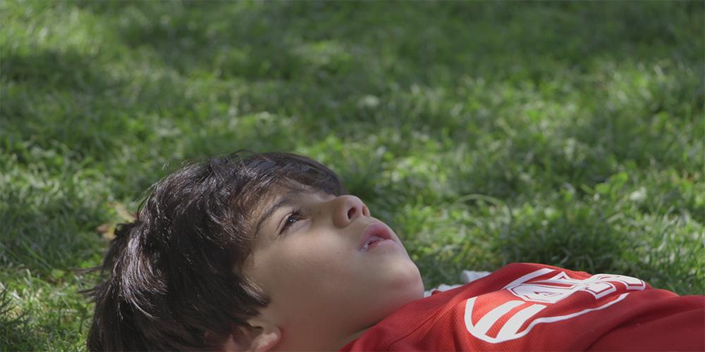 Young Iranian boy lays on the grass looking up at the sky.