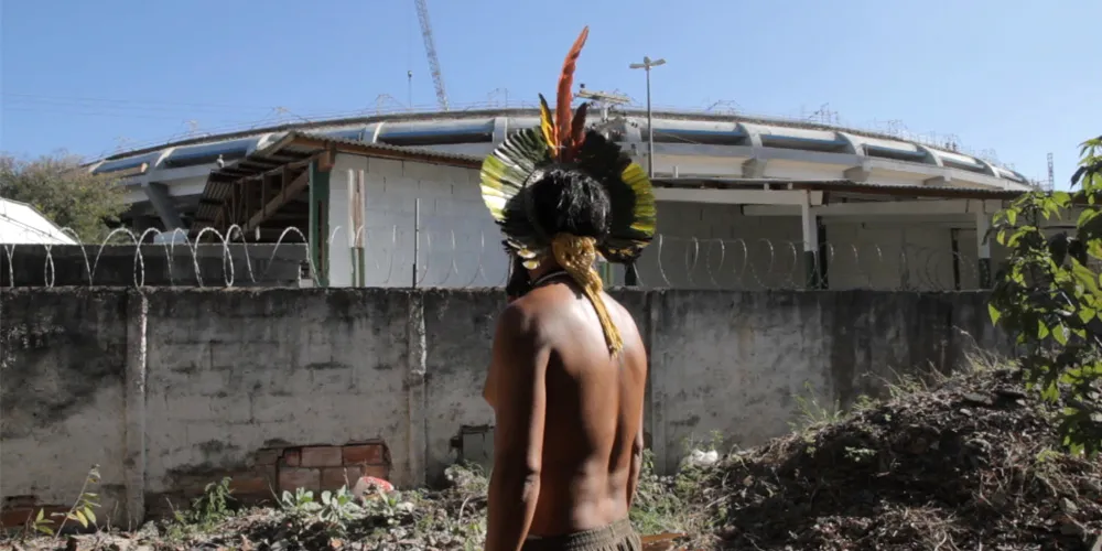A Brazilian in traditional clothing looks at the soccer stadium outside.