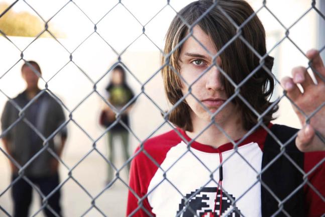 white male teen looks through chainlink fence at school