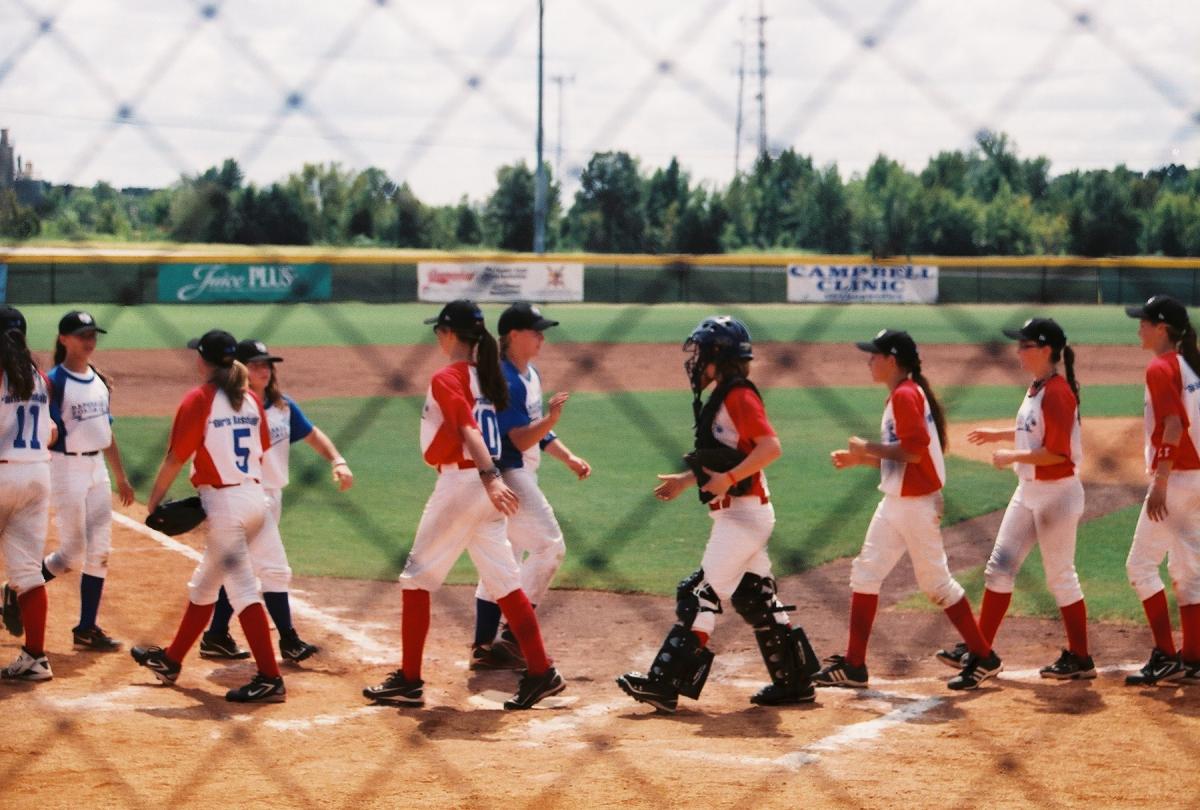 opposing female baseball teams high five in the baseball field at the end of the game.
