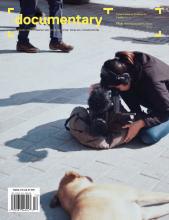 Cover of Spring 2021 issue of Documentary magazine with filmmaker kneeling on the ground, shooting a stray dog, also lying down on its side